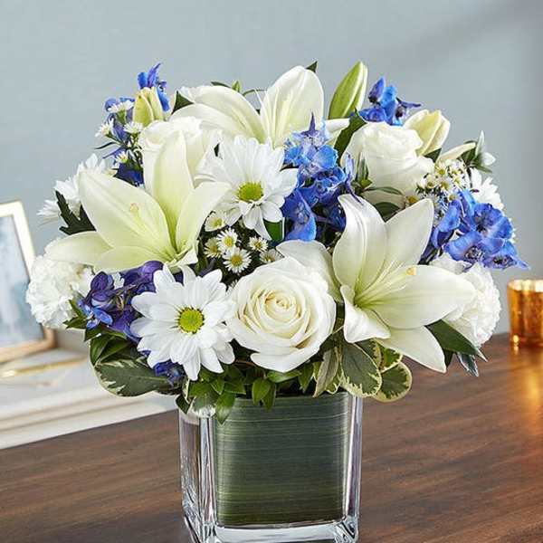 White lilies, roses, and blue flowers in a square glass vase