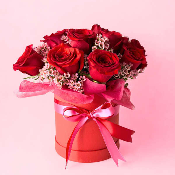 Red roses arranged in a pink hat box with a ribbon bow