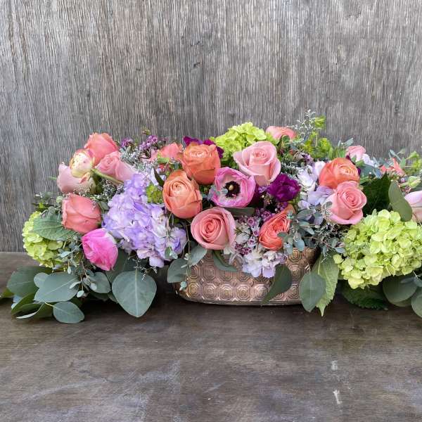Low floral centerpiece with pink and coral roses in a copper vase