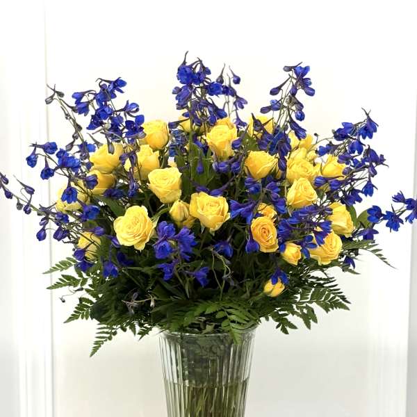Yellow roses and blue flowers in a tall glass vase