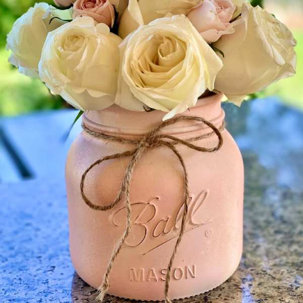 Cream and blush roses arranged in a pink mason jar vase