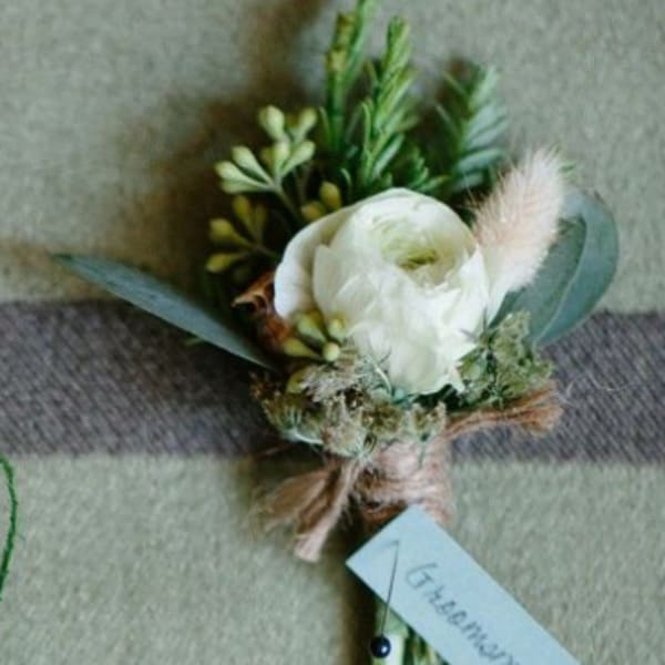 White boutonniere with greenery and a small feather accent