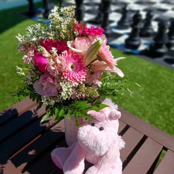 Pink bouquet in a vase beside a plush pink unicorn