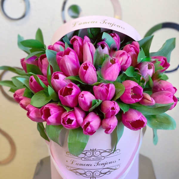 Pink tulips arranged in a round pink hatbox with green leaves