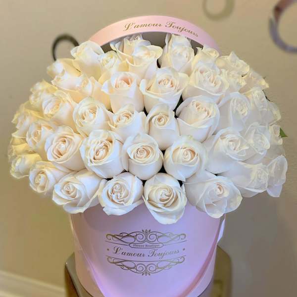 Round box of pale ivory roses densely arranged in a light pink hatbox
