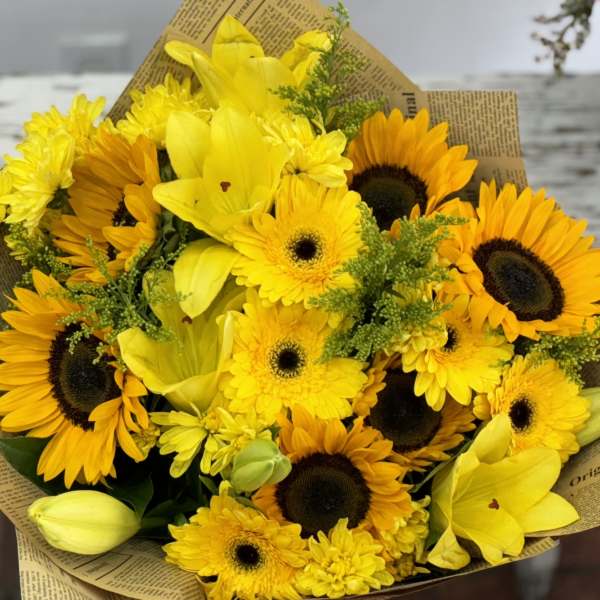 Bouquet of yellow sunflowers and lilies wrapped in newspaper-style paper