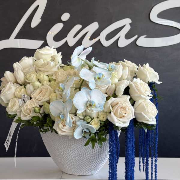 White rose arrangement in a textured white vase with blue orchid accents