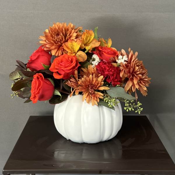 Autumn floral arrangement in a white pumpkin vase with red roses and orange mums