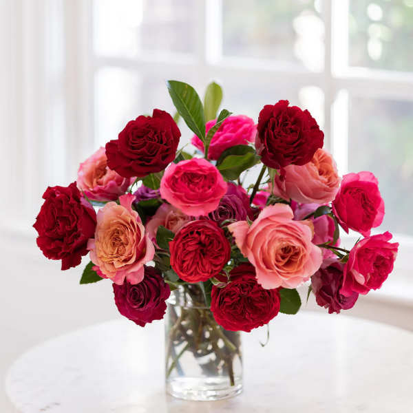 Bouquet of red, pink, and peach roses in a clear glass vase