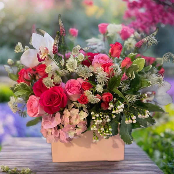 Pink and red roses arranged in a peach box with white accent flowers