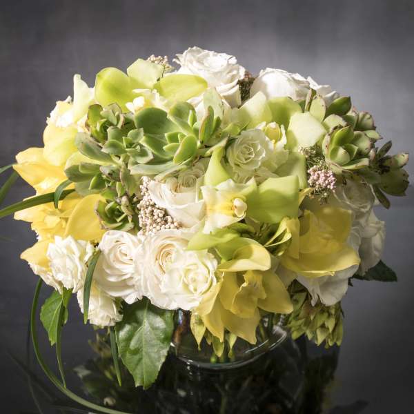 Bouquet of white roses and yellow calla lilies with succulents in a glass vase