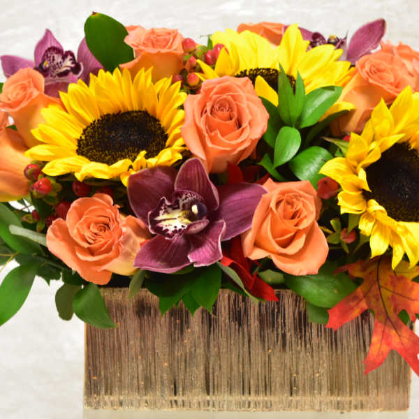 Sunflowers and peach roses in a rectangular vase with purple orchids