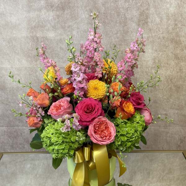 Colorful bouquet of pink, orange, and yellow flowers in a green box with a gold ribbon
