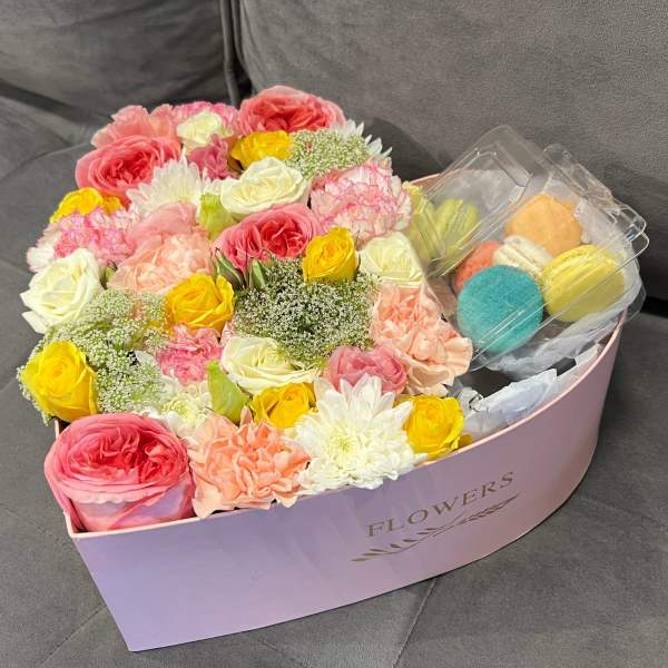 Box of pink, yellow, and white flowers with macarons