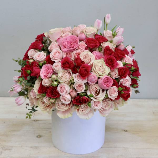 Large arrangement of red and pink roses with tulips in a white cylinder vase