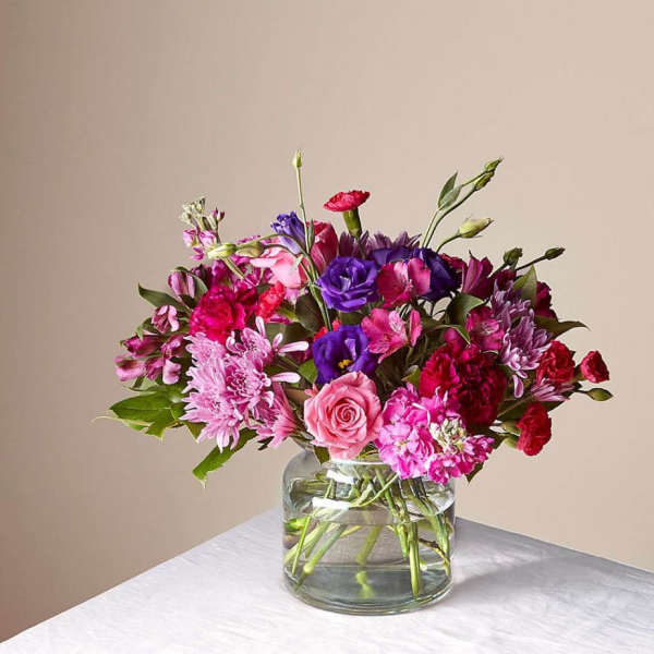 Mixed pink and purple flowers arranged in a clear glass vase