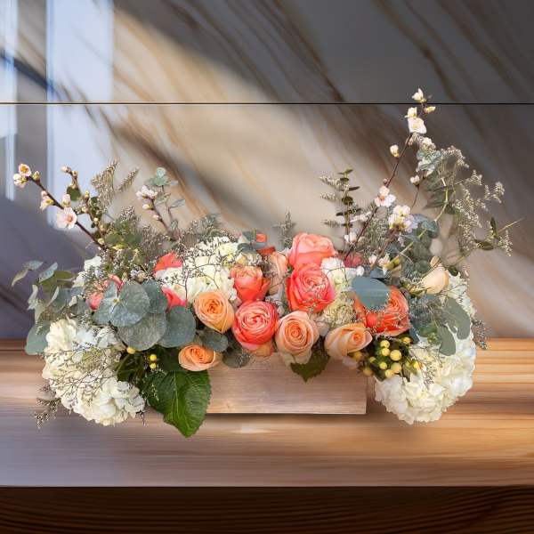 Low floral arrangement of peach and white roses with eucalyptus in a wooden box