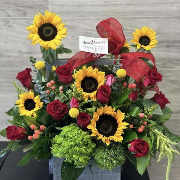 Sunflowers and red roses arranged with a red ribbon in a square container