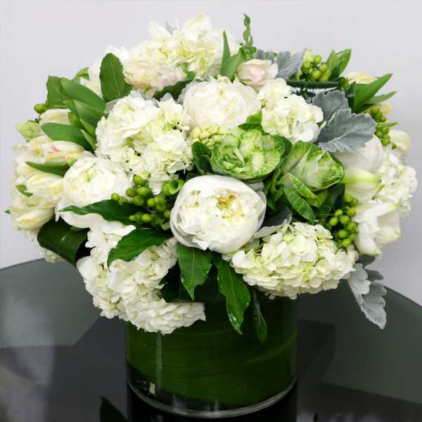 Round arrangement of white peonies and hydrangeas with green accents in a low glass cylinder vase