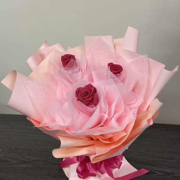 Bouquet of three pink roses wrapped in pale pink paper