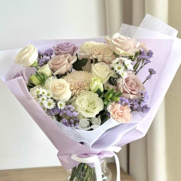 Bouquet of pastel roses, chrysanthemums, and small white daisies in lavender wrap