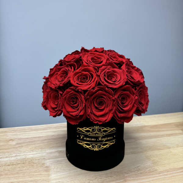 Dome of red roses arranged in a black round hat box on a wooden table.