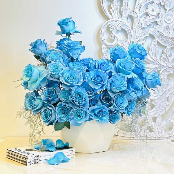 Blue rose arrangement in a white vase with a Chanel book stack