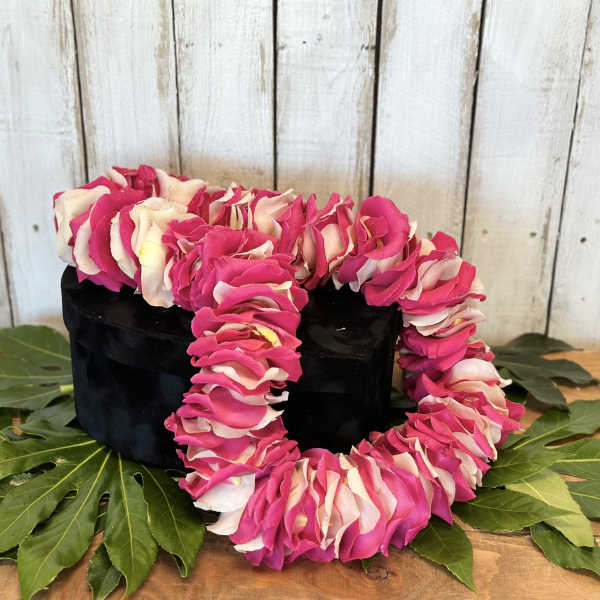 Pink and white flower lei draped over a black box on green leaves