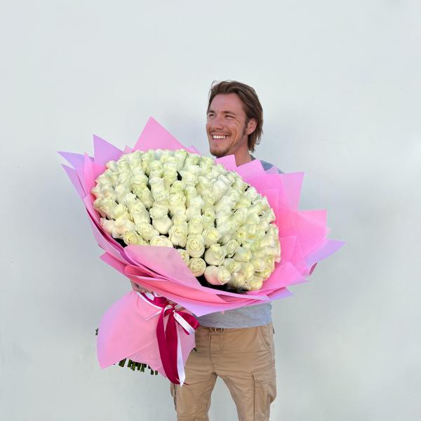 Man holding an oversized bouquet of white roses wrapped in bright pink paper