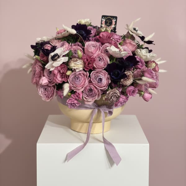 Pink and purple bouquet in a round box with a lavender ribbon