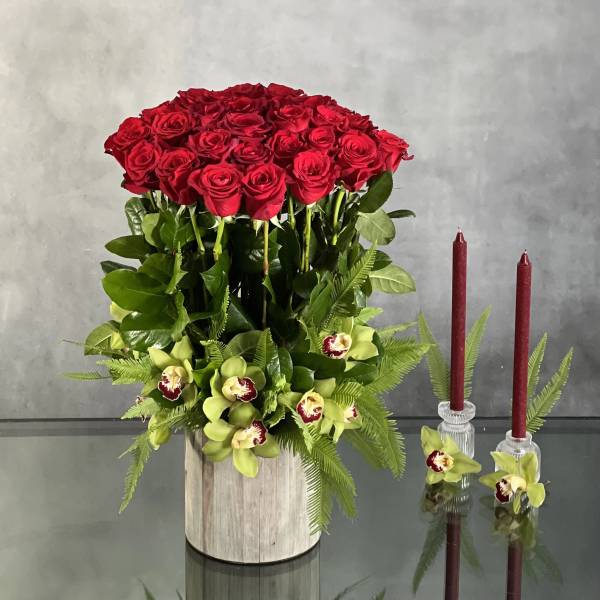Red roses in a wooden container with green orchids and ferns