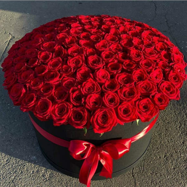 Large black hat box filled with tightly packed red roses and tied with a red satin bow.