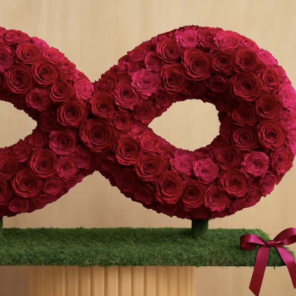 Two red rose wreaths on a grass-covered base with pink ribbons