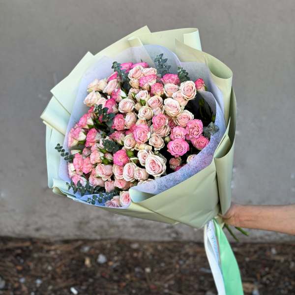 Hand-tied bouquet of pink and blush roses wrapped in pale green paper