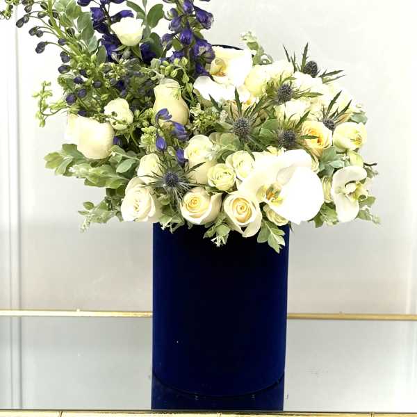 White roses and orchids in a tall navy vase with blue delphinium spikes