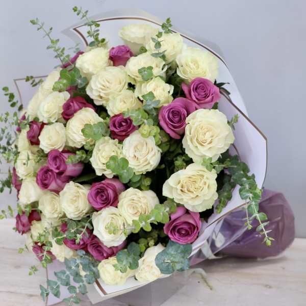 Large bouquet of cream and magenta roses with trailing eucalyptus, wrapped in white paper.
