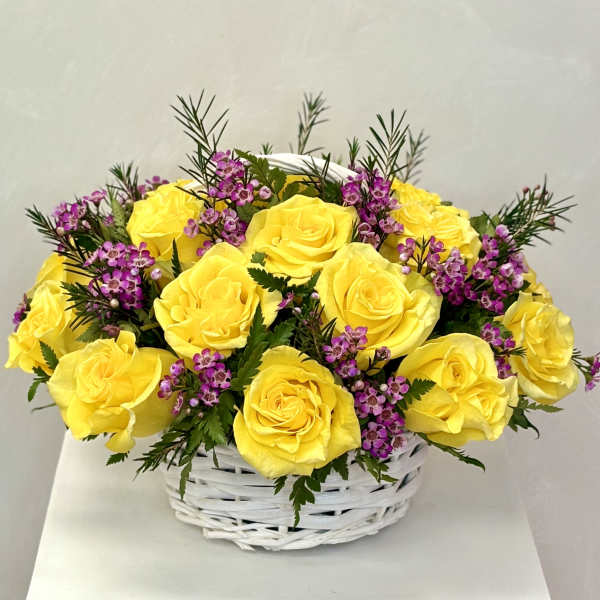 Yellow roses and purple filler flowers in a white basket