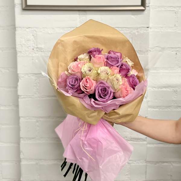 Bouquet of pink, purple, and cream roses wrapped in tan and pink paper