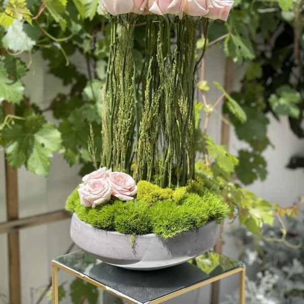 Pink roses arranged in a tall moss-filled bowl with hanging greenery