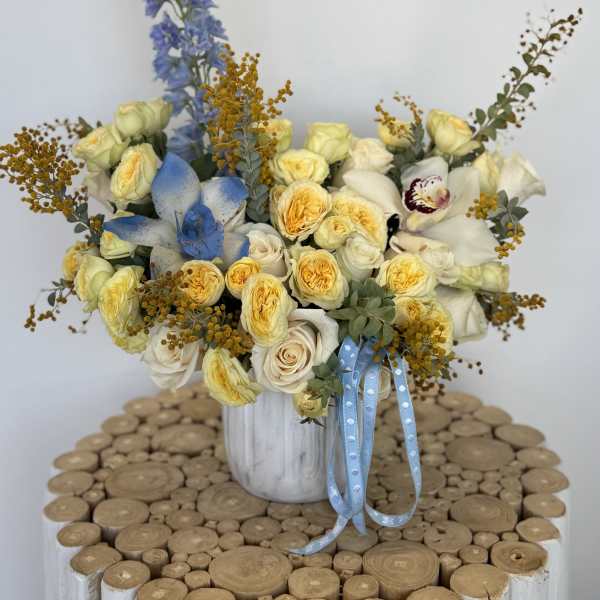 Bouquet of pale yellow and white roses in a white vase with blue ribbon
