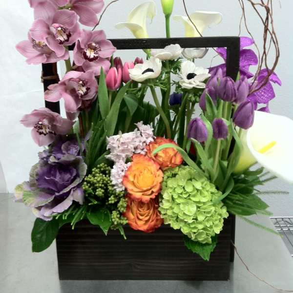 Mixed floral arrangement in a dark rectangular container with orchids and calla lilies