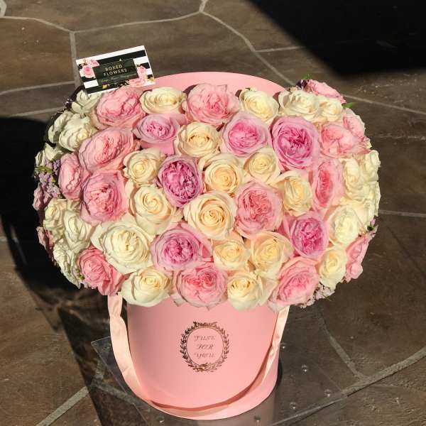 Pink and cream roses arranged in a round pink hat box