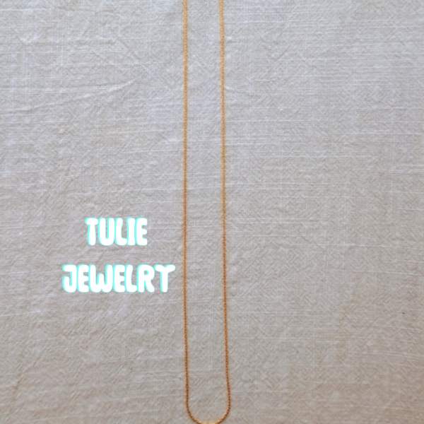 A thin gold necklace laid flat on a light fabric background.