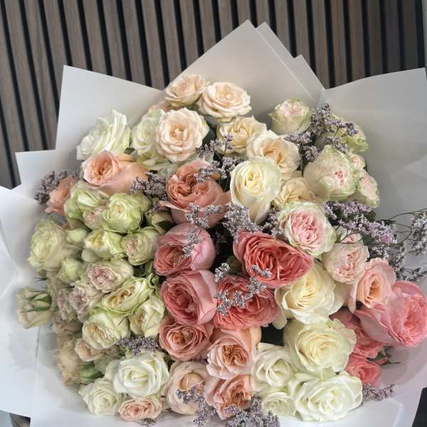 Large bouquet of pastel roses with purple filler flowers in white wrap