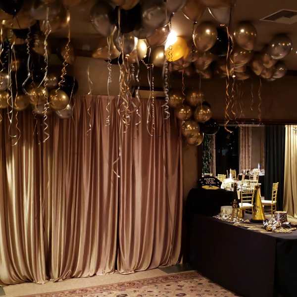Gold and black balloons with curling ribbons over a draped party backdrop