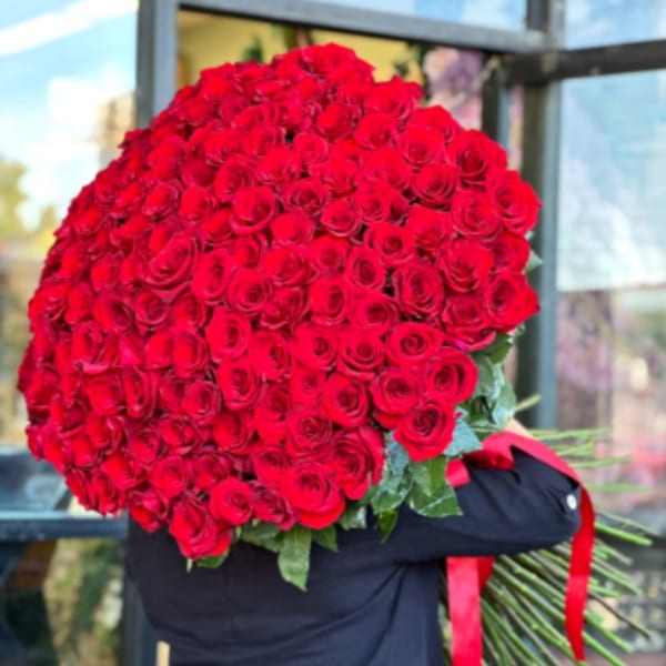 Large bouquet of red roses wrapped in dark paper with a red ribbon