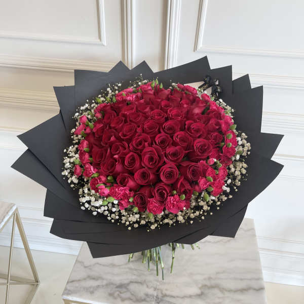Large bouquet of red roses with pink carnations and white baby's breath in black wrap