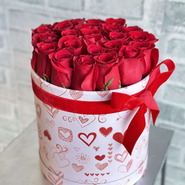 Red roses arranged in a heart-patterned round box with a red ribbon