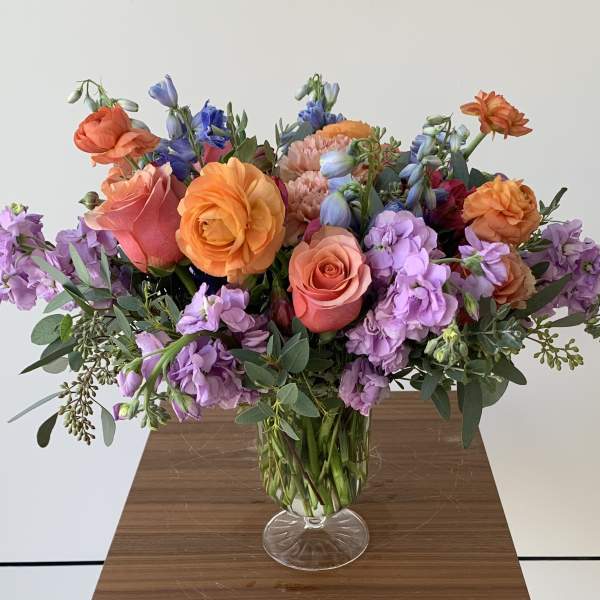Colorful bouquet of roses, ranunculus, and purple blooms in a glass vase