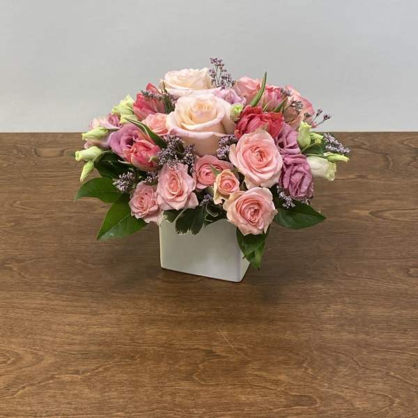 Pink and peach roses arranged in a white square vase